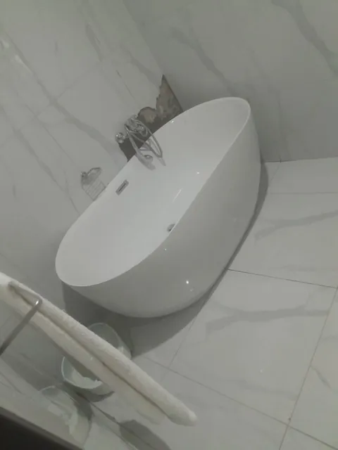 Freestanding oval bathtub with chrome wall mixer on marble-look tiles during a bathroom renovation