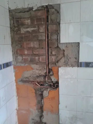 Copper mixer valve and pipes exposed behind a partially demolished tiled bathroom wall