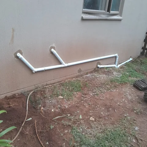 White PVC conduit exiting a grey exterior wall through freshly cemented holes