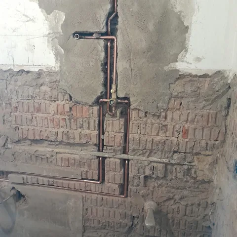 Bright copper piping set into an exposed brick wall during a renovation